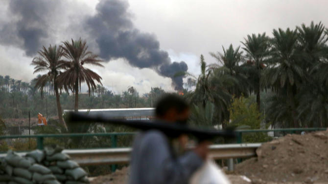 A member of the Iraqi pro-government forces walks in front of flames rising on October 27, 2014, in Jurf al-Sakhr, an area close to Amriyat al-Fallujah, a town that has been hard-pressed by IS in recent weeks