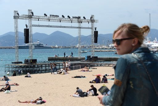 People sit on the beach next to a podium where films will be projected in Cannes