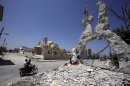 Men ride a motorbike past the remains of a building on August 1, 2013 in front of Saint Elie Church in Qusayr, in Syria's central Homs province