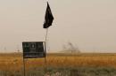 Smoke rises in the distance behind an Islamic State (IS) group flag and banner after Iraqi Kurdish Peshmerga fighters reportedly captured several villages from the IS group in the district of Daquq, south of Kirkuk city, September 11, 2015