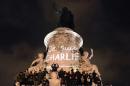 People stand on the statue in Republic square next to graffiti reading "I am Charlie" in Paris on January 7, 2015