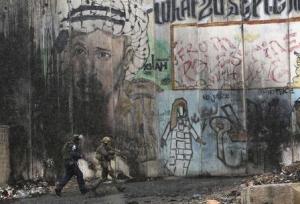 Israeli border policemen walk past a graffiti of the …