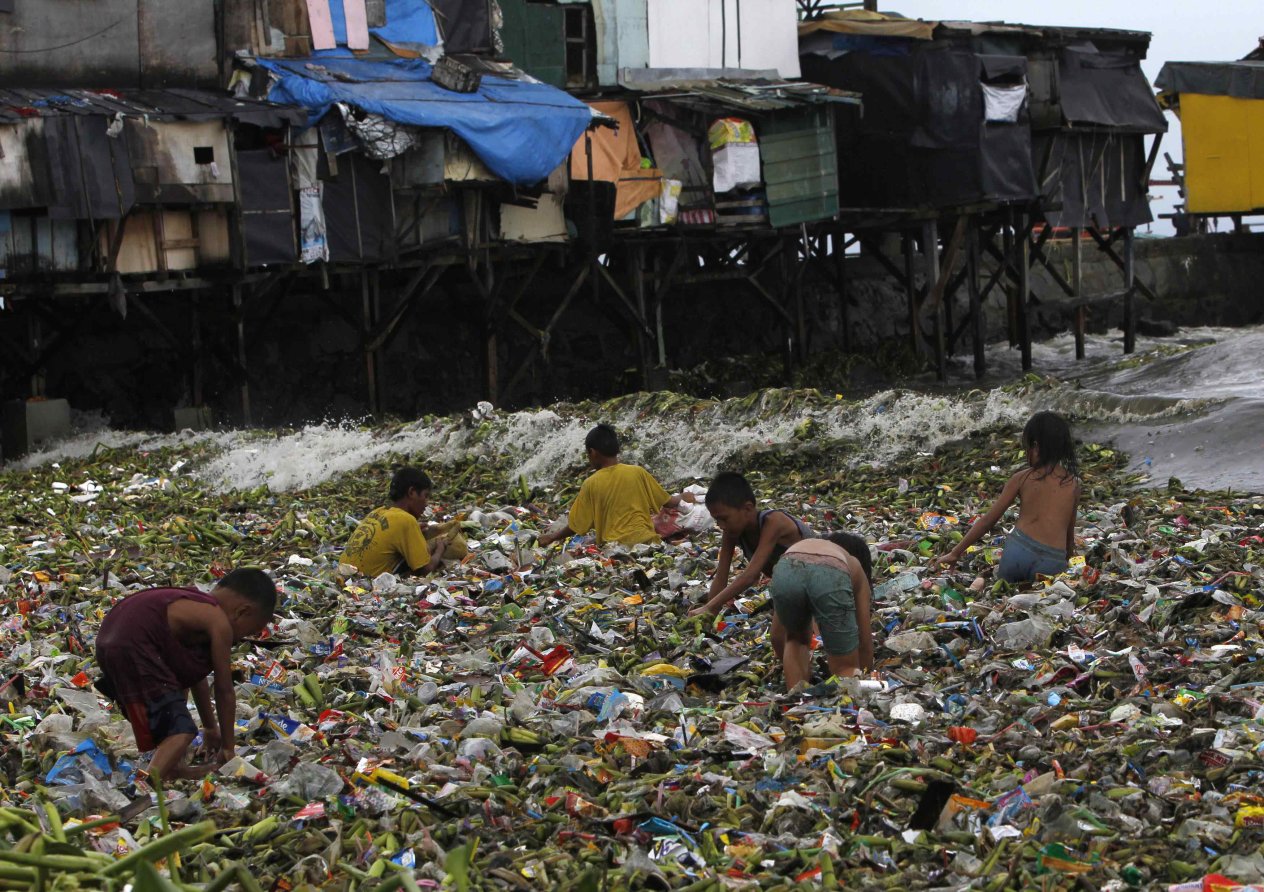 Children sift through floating garbage as they collect recyclable items to sell while strong waves crash along the shores of Manila Bay, near a slum area in Manila