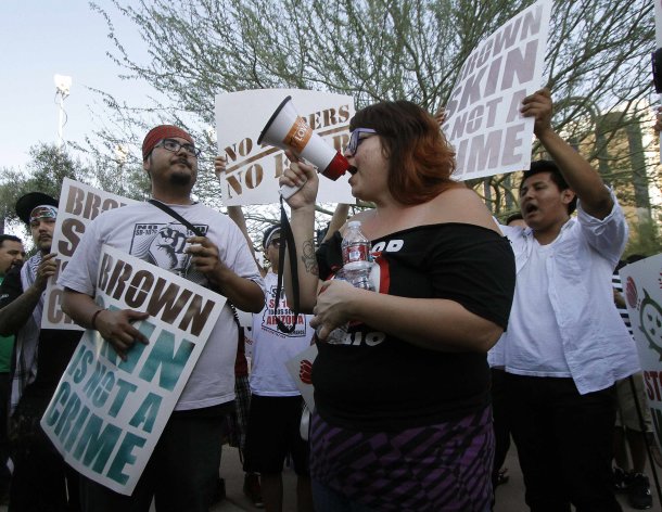 People hold signs as they gather during a protest against Senate Bill 1070 (SB-1070), in front of the Immigration and Customs Enforcement offices in Phoenix, Arizona, June 25, 2012. The U.S. Supreme Court on Monday upheld the main provision of Arizona's crackdown on illegal immigrants but threw out three other parts, handing partial victories to President Barack Obama in his challenge to the law and to the measure's conservative supporters. The court unanimously upheld the statute's most controversial aspect, a requirement that police officers check the immigration status of people they stop, even for minor offenses such as jay-walking. REUTERS/Darryl Webb (UNITED STATES - Tags: POLITICS SOCIETY IMMIGRATION CIVIL UNREST)