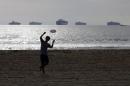 Micah Young catches a frisbee on the beach Friday, Feb. 20, 2015, in Sunset Beach, Calif., as loaded cargo ships are anchored outside the Ports of Long Beach and Los Angeles. Billions of dollars of cargo are sitting on dozens of massive ships anchored outside West Coast ports. They cannot dock because of historically bad cargo bottlenecks at 29 ports that handle about $1 trillion of trade annually, much of it with Asia. (AP Photo/Jae C. Hong)