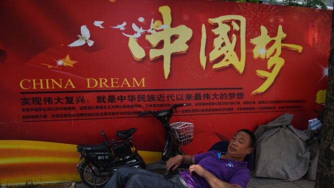 A man rests in Beijing on July 7, 2015, in front of a banner about President Xi Jinping&#39;s vision for China&#39;s future, with characters translating as &quot;To realise the revitalisation is the biggest dream in modern times of Chinese nationals&quot;