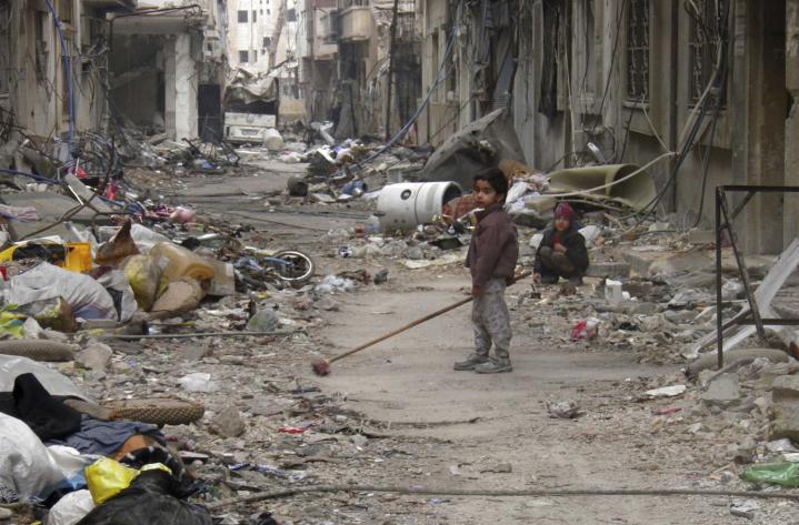 A child clears damage and debris in the besieged area of Homs