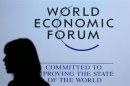 A delegate is silhouetted as she passes by a sign for WEF in Davos