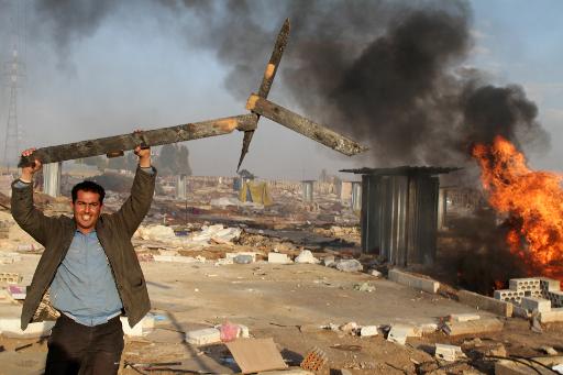 A man holds up a broken wooden structure in a burnt makeshift Syrian refugee camp after it was attacked by residents of the neighbouring Lebanese village Qsar Naba on December 2, 2013