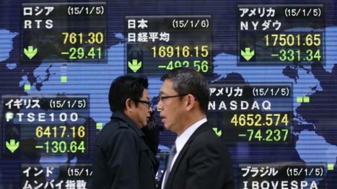 Passersby walk past in front of an electronic board displaying Japan's Nikkei average and various countries' stock price index outside a brokerage in Tokyo
