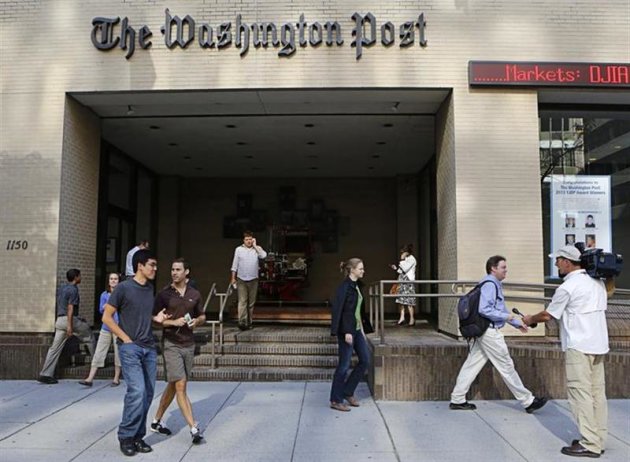 A television cameraman takes up a position as people walk by the entrance of the Washington Post headquarters in Washington, August 5, 2013. REUTERS/Stelios Varias