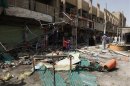 Residents stand amid debris and twisted metal near shops damaged by a car bomb attack that occurred late on Monday in east of Baghdad