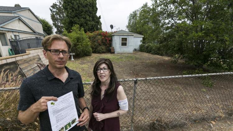 Michael Korte and his wife Laura Whitney, pose outside their home lawn in Glendora, Calif., Thursday, July 17, 2014. The Southern California couple who scaled back watering due to drought received a letter from the city of Glendora warning that they could face fines if they don't get their brown lawn green again. They are told if they don't revive the lawn they could be hit with up to $500 in fines and possible criminal action. City Manager Chris Jeffers says the couple has not been cited and called it a friendly letter prompted by a neighbor's complaint. (AP Photo/Damian Dovarganes)