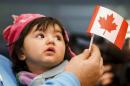 A young Syrian refugee looks up as her father holds her and a Canadian flag at the as they arrive at Pearson Toronto International Airport in Mississauga