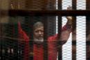 Deposed President Mohamed Mursi greets his lawyers and people from behind bars at a court wearing the red uniform of a prisoner sentenced to death, during his court appearance with Muslim Brotherhood members on the outskirts of Cairo