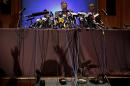 Over a dozen microphones are propped on a table as Malaysian police chief Khalid Abu Bakar answers questions from members of the media, raising their hands waiting their turn as seen in the shadows cast on stage during a press conference, Tuesday, March 11, 2014 in Sepang, Malaysia. One of the two men traveling on a missing Malaysia Airlines jetliner with a stolen passport was a 19-year-old Iranian man believed to be trying to migrate to Germany, and had no terror links, police said Tuesday. (AP Photo/Wong Maye-E)