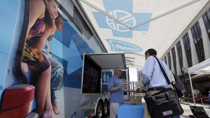 FILE - In this photo taken Wednesday, July 17, 2013, Blue Cross Blue Shield of North Carolina employee Lew Borman, left, helps a customer outside a trailer at the downtown farmer's market in Raleigh, N.C. Dozens of health insurers say higher-than-expected care costs and other expenses blindsided them this year, and they’re going to have to hike individual insurance prices well-beyond 10 percent for 2016. (AP Photo/Gerry Broome, File)