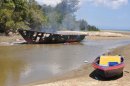 A burnt sampan, a small boat, sits on the beach in Kampung Tanduo