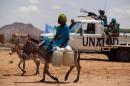 A handout picture taken on June 30, 2014 shows a woman riding a donkey loaded with water jerrycans, while UNAMID troops from Tanzania conduct a routine patrol in the camp for internally displaced persons in Khor Abeche, South Darfur