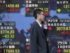 A man passes an electronic board displaying market indices from around the world outside a brokerage in Tokyo