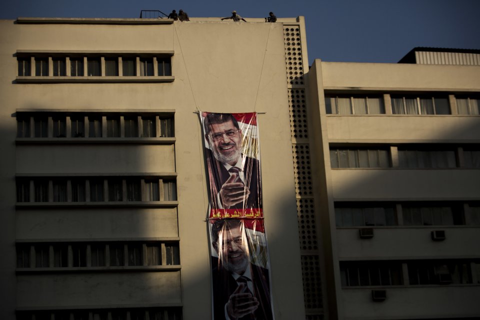 Supporters of Egypt's ousted President Mohammed Morsi rise a banner with his portrait during a protest outside the Republican Guard building in Cairo, Egypt, Sunday, July 7, 2013. Egypt's new leadership wrangled over the naming of a prime minister, as both the Muslim Brotherhood and their opponents called for new mass rallies Sunday, renewing fears of another round of street violence over the military's ousting of Islamist President Mohammed Morsi. The calls for competing rallies come after clashes two days ago between the rival camps left at least 36 dead and more than 1,000 injured nationwide .(AP Photo/Manu Brabo)