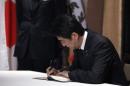 Japan's PM Abe signs a condolences book as he pays respects for victims of the attack at Charlie Hebdo, during a visit to the French Ambassador's residence in Tokyo
