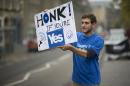 David Aguilar from Catalonia, who is visiting Scotland to support the Scottish independence referendum, holds up a placard supporting a Yes vote at passing motorists in Edinburgh, Scotland, Thursday, Sept. 18, 2014. Polls have opened across Scotland in a referendum that will decide whether the country leaves its 307-year-old union with England and becomes an independent state. (AP Photo/Matt Dunham)