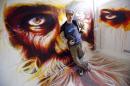 French artist Dan23 poses front of his paintings in a social housing tower converted into a temporary street art exhibition in Paris, France, Tuesday, Oct. 8, 2013. Condemned apartments never looked so good _ and only rarely has graffiti met such an enthusiastic welcome. More than 80 artists were given free run of a rundown building that is doomed to destruction in 8 days. The line wraps around the block every day to see the apartments, each of which is its own art installation. (AP Photo/Francois Mori)