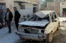 Residents stand near a damaged car in the town of Darat Izza, province of Aleppo