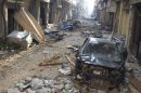A damaged car and houses are seen in Homs