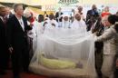 FILE- In this Saturday, Feb. 20, 2010, file photo, former British Prime Minister Tony Blair, left, former Nigerian President Olusegun Obasanjo, on Blair's left, and Religion Leaders hold a Mosquito net with a women lying inside to demonstrate the use of the net against malaria in Abuja, Nigeria. The operation to fight Ebola in West Africa has hampered the campaigns against malaria, a preventable and treatable disease that is claiming many thousands of lives. In information released Sunday Dec. 28, 2014, Dr. Bernard Nahlen, deputy director of the U.S. President's Malaria Initiative says they have had to stop pricking fingers to do blood tests for malaria, so statistics show a decrease in reported cases of maleria but the decrease is likely because people are too scared to go to health facilities and are not getting treated for malaria.(AP Photo/Sunday Alamba, FILE)