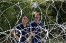 Hungarian police officers guard behind barbed wire near Morahalom, Hungary, Thursday, July 16, 2015. A fence on Hungary's border with Serbia to stem the flow of migrants and refugees will be complete by Nov. 30, the Hungarian defense minister said Thursday. Csaba Hende said that 900 people would work to install the fence, which is planned to be 4 meters (13 feet) high along the 175-kilometer (109-mile) border between Hungary and Serbia. (AP Photo/Darko Vojinovic)