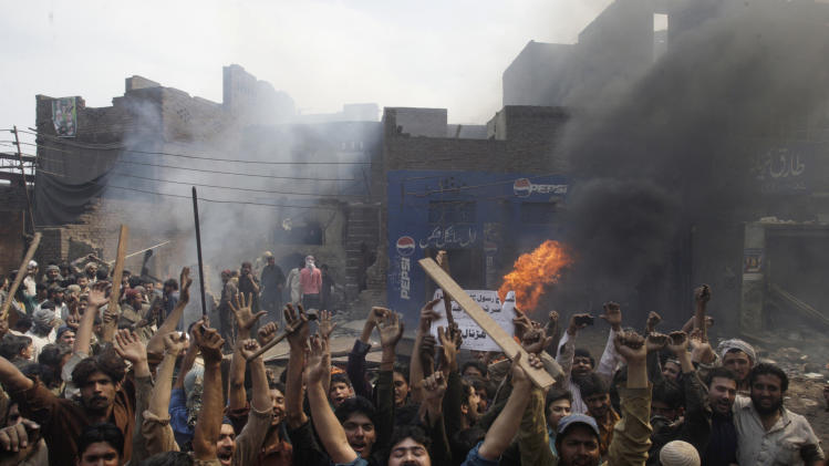 An angry mob reacts after burning Christian houses in Lahore, Pakistan, Saturday, March 9, 2013. A mob of hundreds of people in the eastern Pakistani city of Lahore attacked a Christian neighborhood Saturday and set fire to homes after hearing accusations that a Christian man had committed blasphemy against Islam's prophet Mohammed, said a police officer. Placard center reads, " Blasphemer is liable to death." (AP Photo/K.M. Chaudary)