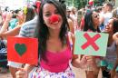 Luiza Rocha, a 22-year-old university student, holds up placards with symbols used on the hookup app Tinder at the Tinder-themed debut street party "Match Comigo" in Rio de Janeiro, Brazil, Monday, Feb. 16, 2015. The heart symbol on the app is tapped to show that you like a suggested match and the X symbol is used decline the match. The brainchild of a 28-year-old publicist who says he's 