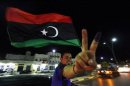 A man, with an inked finger, flashes the victory sign as he celebrates with the new Libyan flag at the end of voting day in Sirte