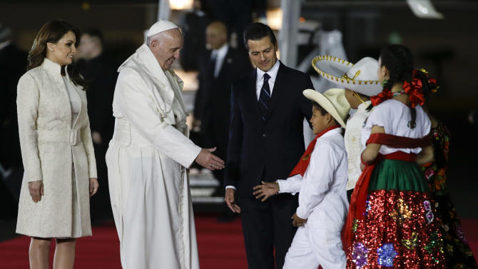 Pope Francis reaches out to greet youth dressed in traditional Mexican outfits as he's escorted by Mexico's President Enrique Pena Nieto, behind, and first lady Angelica Rivera, upon arrival to Benito Juarez International Airport in Mexico City, Friday, Feb. 12, 2016. The pontiff is in Mexico for a week-long visit. (AP Photo/Gregorio Borgia)