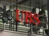 People walk behind the logo of Swiss bank UBS in Zurich