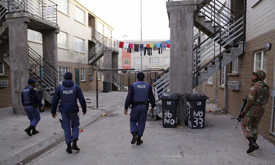 A South African soldier, right,  provide security for  policemen, left,  as they look for drugs in  Manenberg, South Africa,  Thursday, May 21, 2015. ...
