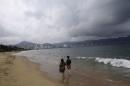 Tourists walk along a beach as dark clouds brought by hurricane Blanca are seen in Acapulco