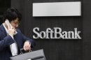 A man using a mobile phone walks past a SoftBank Corp branch in Tokyo