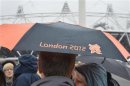 A spectator shelters under an umbrella with a London 2012 Olympics logo in the Olympic Park at Stratford, east London