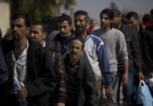 Men wait to be searched by the Syrian military after …