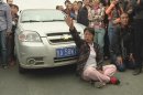 A woman sitting in front of a car shouts during a protest by families outside a poultry slaughterhouse where a blaze broke out on Monday, in Dehui