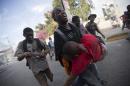 An opposition protester carries a fellow demonstrator injured by a machete when he was attacked by a resident in a neighborhood known for it's support of the ruling party, during a protest march against official preliminary election results, in Port-au-Prince, Haiti, Friday, Nov. 20, 2015. Residents began throwing rocks at marchers as they made their way through the neighborhood. One protester was killed by a gunshot, when police intervened in the clashes between the residents and protesters. The presidential runoff election is Dec. 27. (AP Photo/Dieu Nalio Chery)