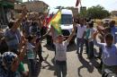 Kurdish people waving flags flash the V-sign and applaud while lining the road, as the convoy carrying the body of US citizen, Keith Broomfield, killed in fighting with the militants of the Islamic State group in Kobani, Syria, is driven by through Suruc, on the Turkey-Syria border, Thursday, June 11, 2015. Keith Broomfield, 20 from Massachusetts, died June 3 in battle in a Syrian village near Kobani, making him likely the first U.S. citizen to die fighting alongside Kurds against the Islamic State group. (AP Photo/Lefteris Pitarakis)