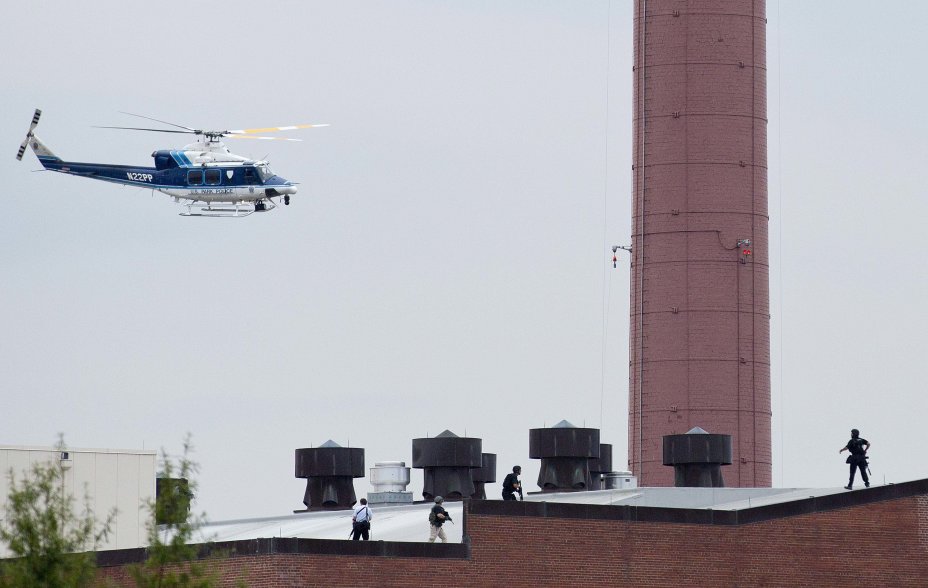 A police helicopter is seen as police walk on the roof of a building as they respond to a shooting at the Washington Navy Yard, in Washington