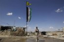 A Free Syrian Army fighter carrying his weapon, walks along a street as Syrian opposition and Popular Protection Units flags flutter, in Aleppo's Sheikh Maqsoud neighbourhood