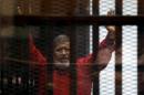 Egypt's deposed president Mohamed Mursi greets his lawyers and people from behind bars at a court wearing the red uniform of a prisoner sentenced to death, during his court appearance with Muslim Brotherhood members on the outskirts of Cairo
