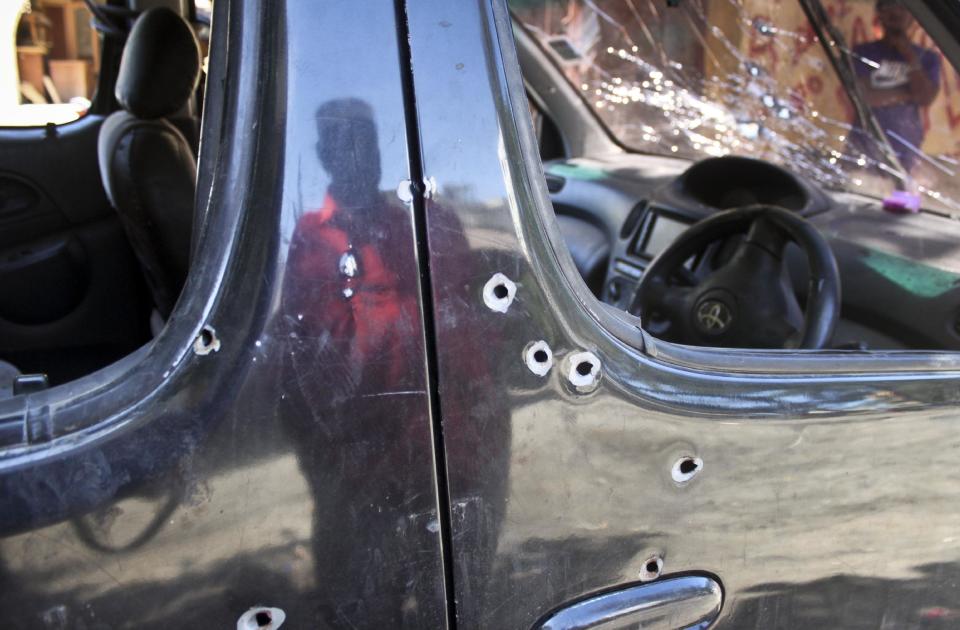 In this photo taken Tuesday, Oct. 29, 2013, Mohamed Hamoud, the 70-year-old father of the slain driver of the car in which Sheik Ibrahim Ismael was killed in early October, is reflected in the doors of the bullet-riddled car at his son's wood shop in Mombasa, Kenya. (AP Photo/Jason Straziuso)