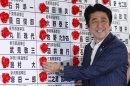 Japanese Prime Minister Shinzo Abe smiles as he places a red rosette on the name of his Liberal Democratic Party's winning candidate during ballot counting for the upper house elections at the party headquarters in Tokyo Sunday, July 21, 2013. Japanese broadcasters projected that Abe's ruling coalition won a majority of seats in the upper house of parliament in elections, giving it control of both chambers for the first time in six years. (AP Photo/Shizuo Kambayashi)